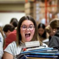 Student holding stack of books with excited smile